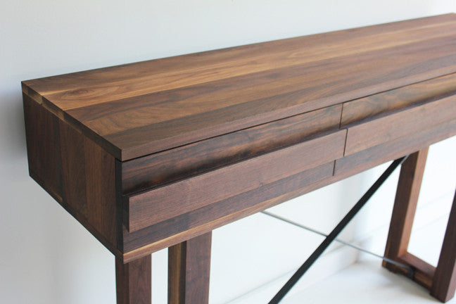 Close-up angled view of the Console Table's solid walnut top and drawer, showing the wood grain and X-braced iron stretcher